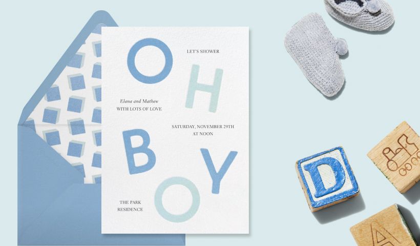 A white invitation with blue letters spelling ‘OH BOY’ on a blue backdrop with wooden blocks and baby booties. 