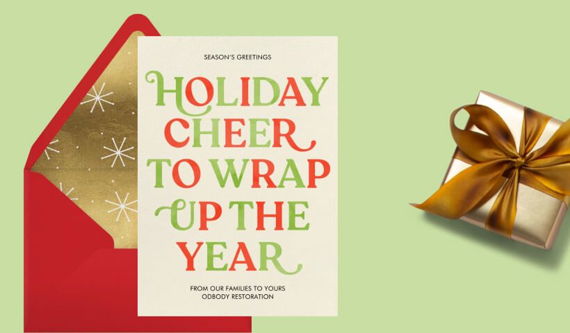 A holiday card in alternating green and red lettering that reads ‘holiday cheer to wrap up the year’ set on a red envelope with gold, starry liner on a green background with a small wrapped gift. 