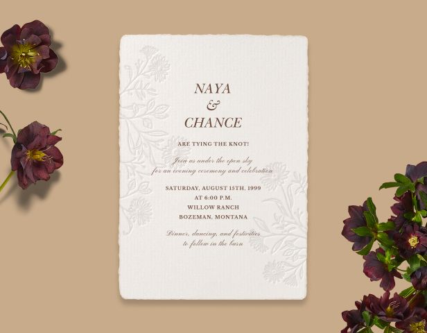 A tan background with dark red flowers paired with a floral embossed wedding invitation with a ripped edge border.