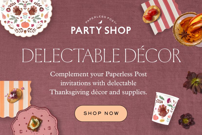 A dusty rose background is styled with floral-patterned plates and cups, striped napkins, appetizers, and an autumn cocktail. White text invites viewers to complement Paperless Post invitations with Thanksgiving décor and supplies, above a peach-colored “Shop Now” button.