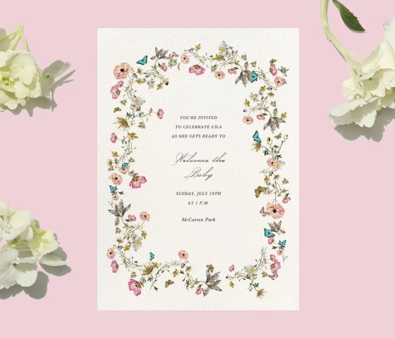 A white invitation with colorful flowers and butterflies on a pink backdrop with white flowers.