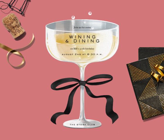 A coupe glass-shaped invitation on a pink backdrop with napkins and a cork.