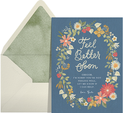 A blue card with a wreath of flowers and white cursive text reading 'Feel Better Soon'. 