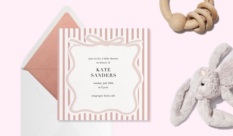 A pink striped invitation with a ribbon border on a pink backdrop with a stuffed bunny and wooden toy. 