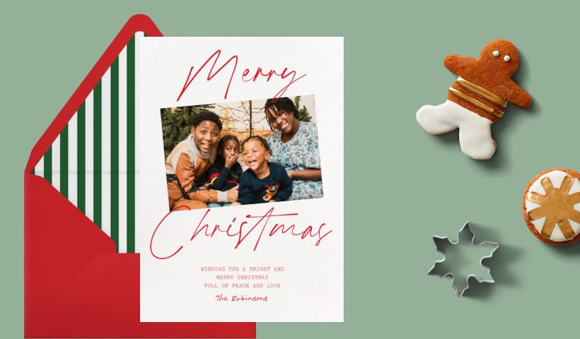 A photo card that reads ‘Merry Christmas’, set on a red envelope with a green and white striped liner, on a sage background with gingerbread cookies and snowflake cookie cutter. 