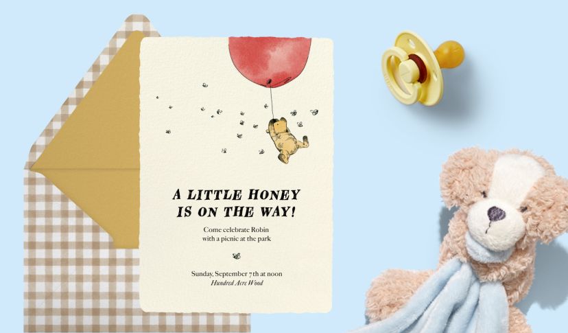 Baby shower invitation featuring a bear holding a red balloon, paired with a gingham envelope, pacifier, and plush toy on a pale blue background.