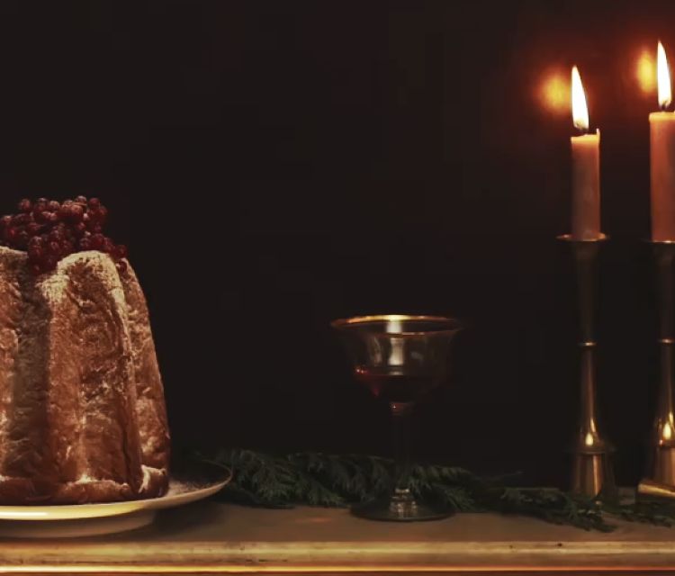 Un fondo de color marrón oscuro en el que se ven velas, bebidas y postres festivos. En la parte izquierda de la pantalla, una invitación para las fiestas dentro de un cuadrado verde. 